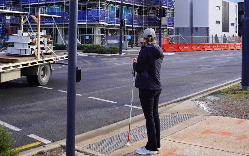 Cassie is pictured holding her cane and waiting for the pedestrian light to change