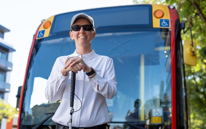 Cassie-Hames-in-front-of-bus-holding-cane