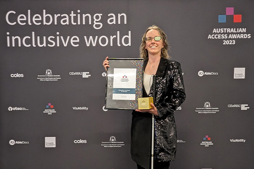 Cassie Hames holding the award for the Initiative of the Year with a banner that reads 'Celebrating an inclusive world' behind her.