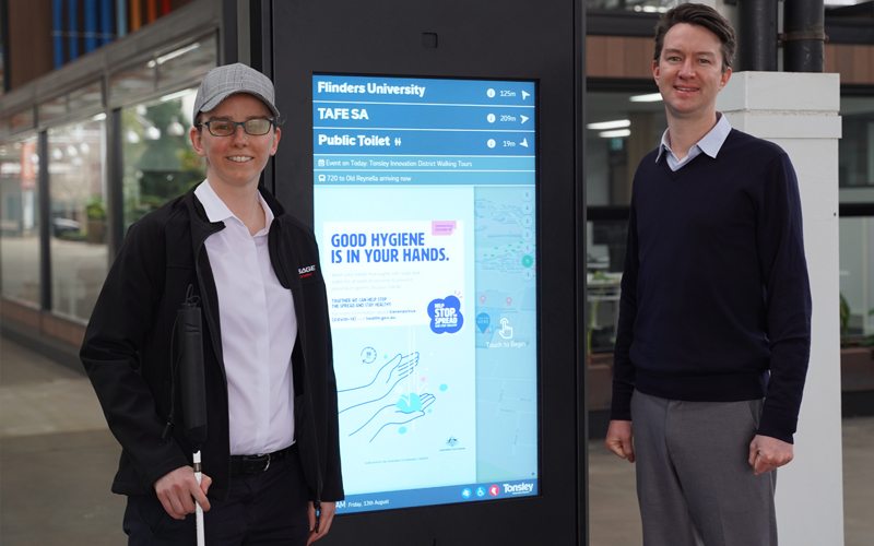 Cassie and Ashby are pictured standing on either side of a digital kiosk